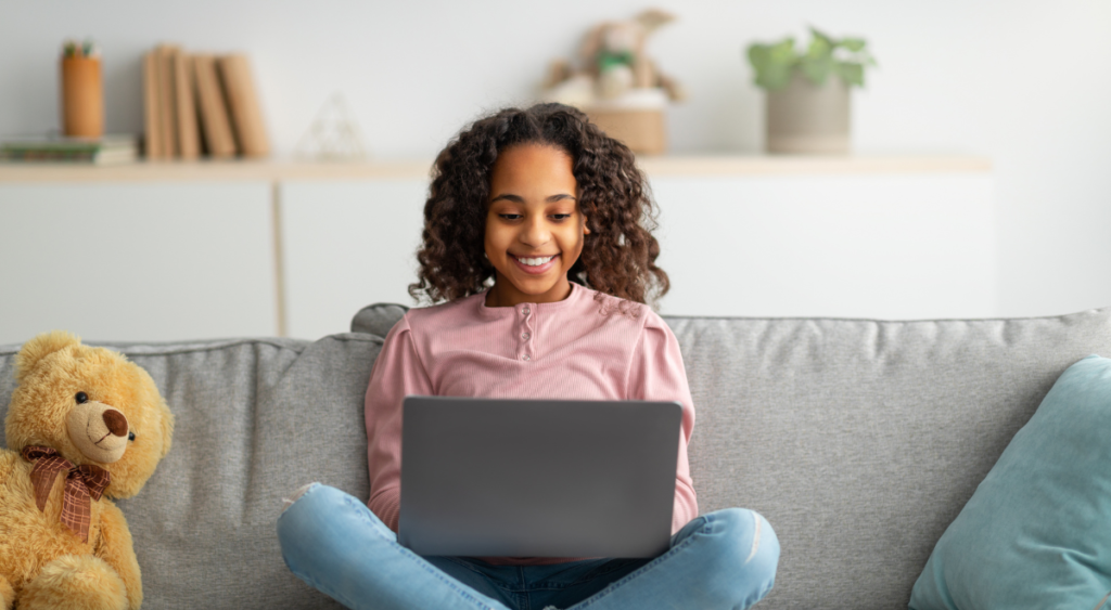 Girl sits on couch with laptop and teddy bear