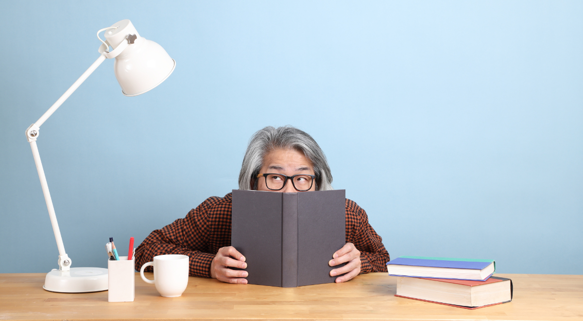 man peeks out from behind a book